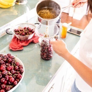 lady pouring pickling liquid over cherries in jar