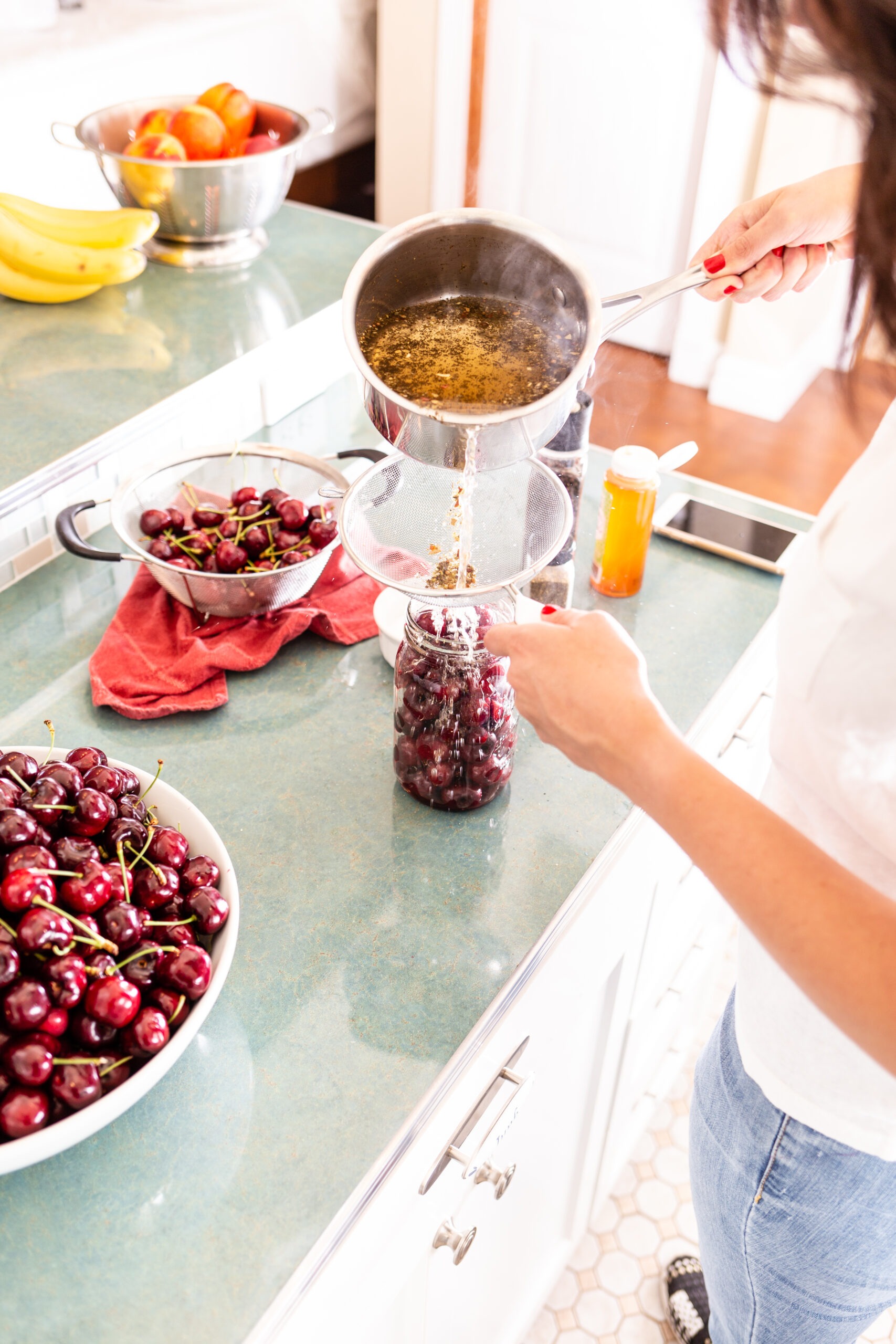 lady pouring pickling liquid over cherries in jar