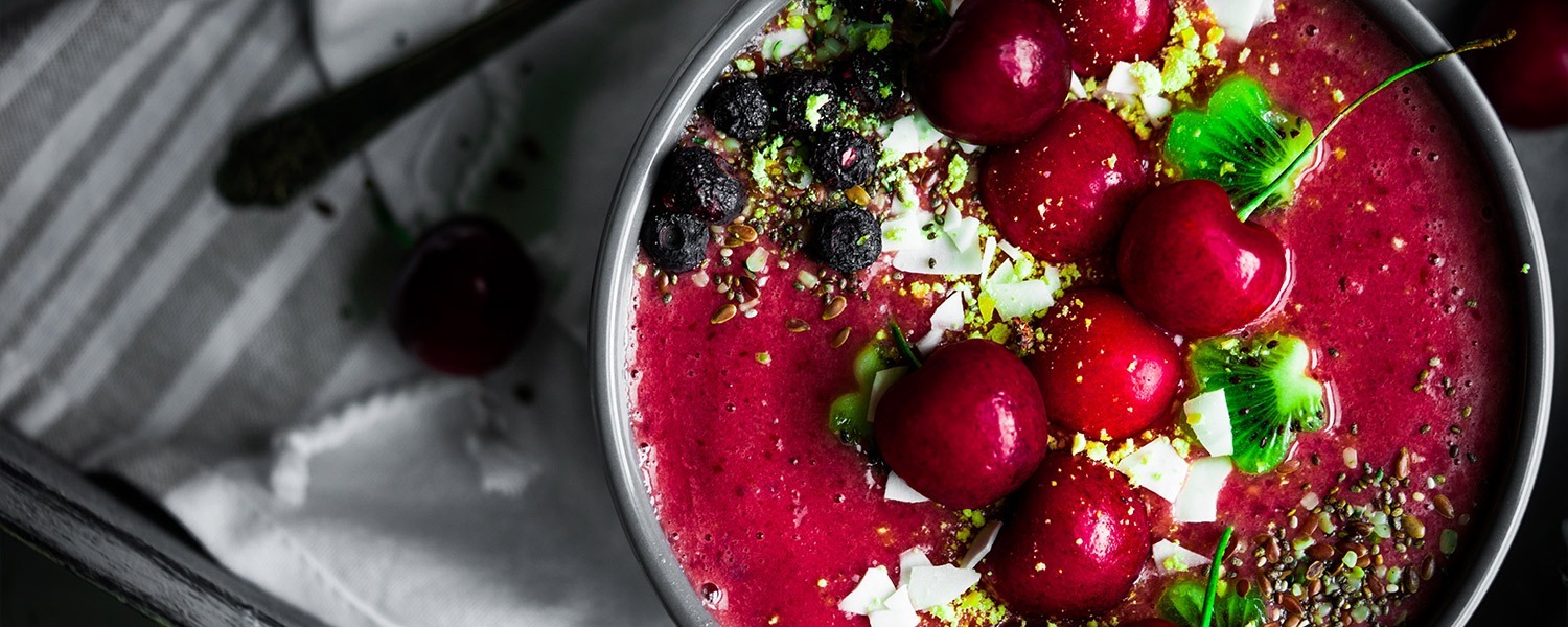 Smoothie bowl with fresh cherries, kiwi, dried blueberries and seeds on top.